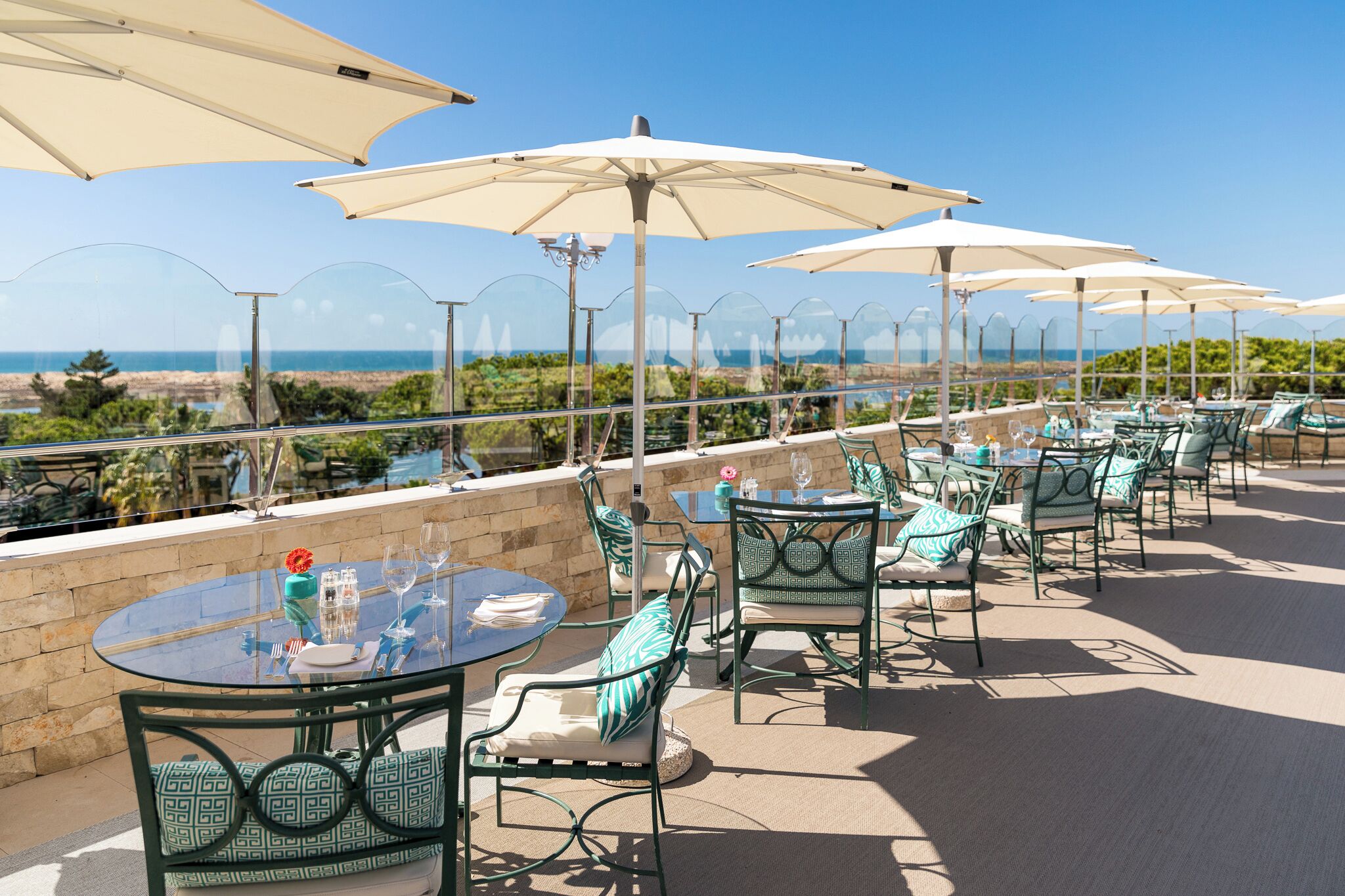 A rooftop terrace with outdoor seating, including round tables and chairs, and large umbrellas providing shade.