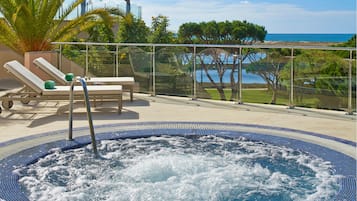 Un jacuzzi con barandilla de cristal, sillones de descanso y vista al mar.