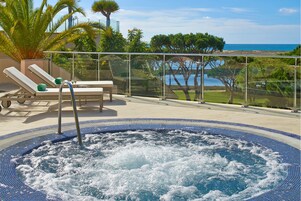 Un jacuzzi doté d’une balustrade en verre, de chaises longues et offrant une vue sur la mer.