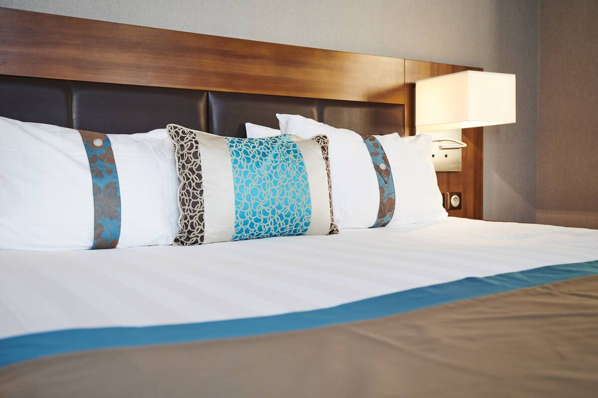 A neatly made bed with a headboard, multiple pillows with patterned designs, and a bedside lamp.