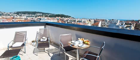 A rooftop terrace with a table set for two, two chairs, and a view of a cityscape.