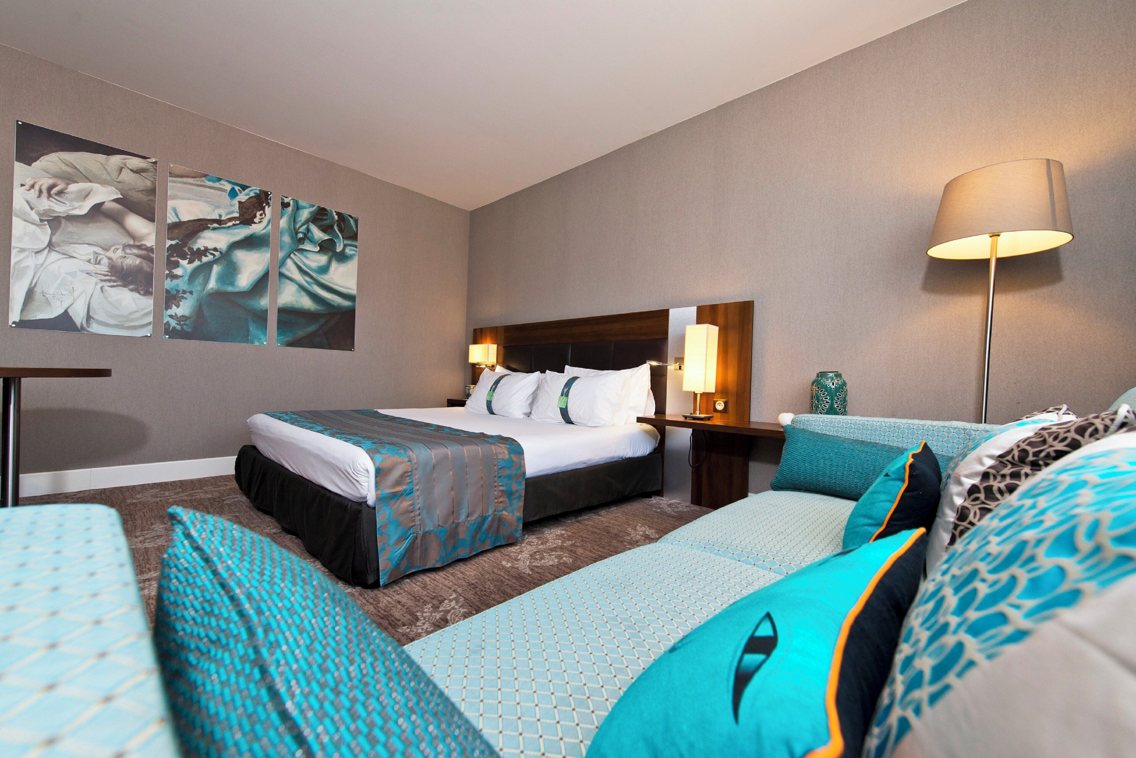A hotel room with a bed, a sofa, a lamp, and artwork on the wall.