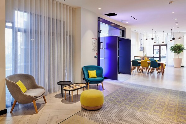 A modern hotel lobby with a seating area, a reception desk, and a large window with curtains.