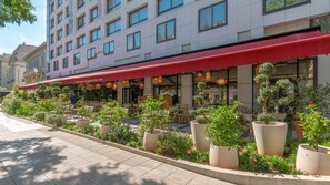 A hotel with a red awning, outdoor seating, and potted plants.