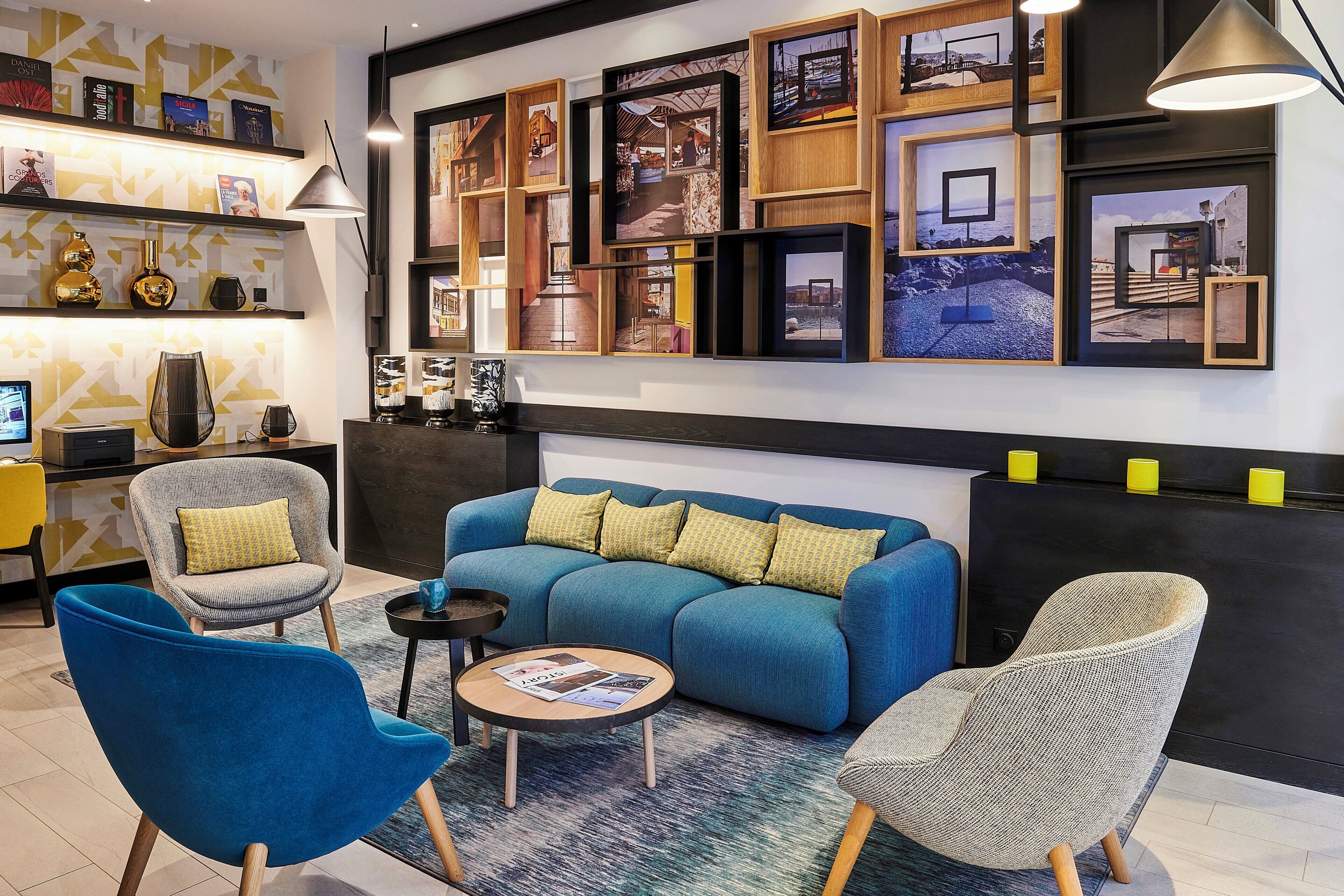 Una sala de estar moderna con un sofá azul, dos sillones, una mesa de centro y una pared decorada con cuadros y libros.