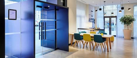 A modern interior with a glass partition, a dining area with wooden chairs, and a large potted plant.