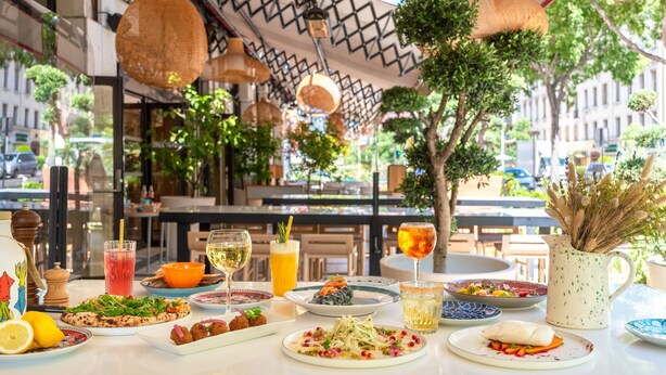 Uma mesa de restaurante com diversos pratos, bebidas e um jarro de flores.