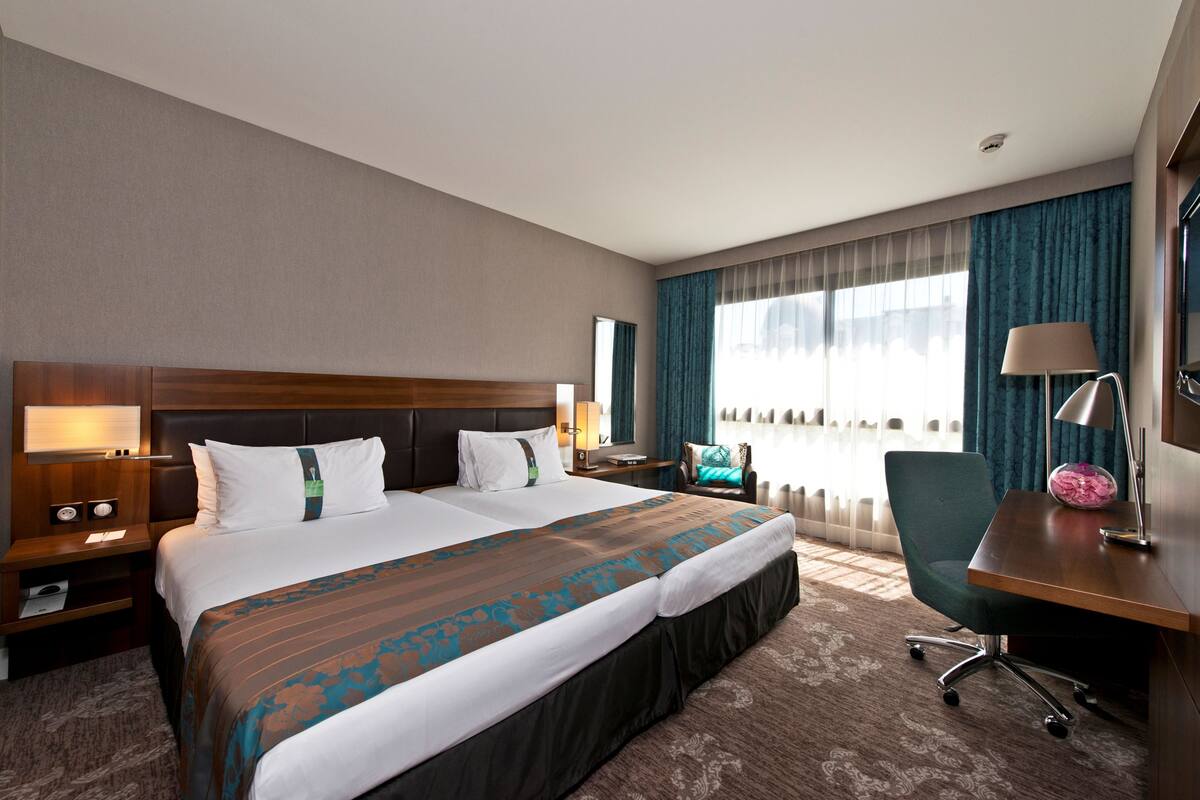A hotel room with a large bed, a desk, a chair, and a view of the city.