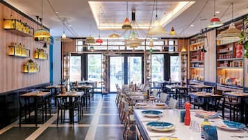 L’intérieur d’un restaurant, avec de nombreuses tables, des chaises et des luminaires suspendus.
