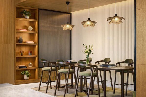 Un espace de salle à manger moderne, avec une bibliothèque en bois, des luminaires suspendus et une table entourée de chaises.