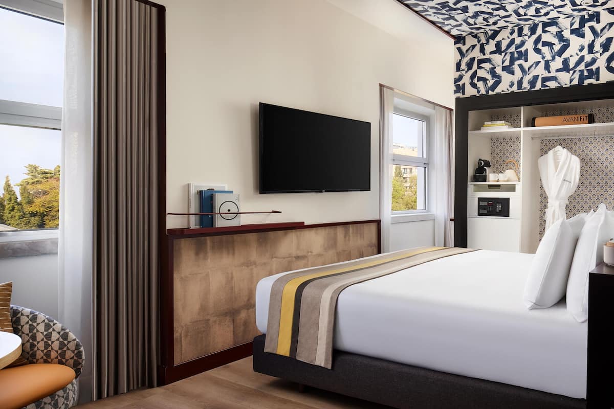 Une chambre d’hôtel dotée d’un grand lit, d’un téléviseur à écran plat fixé au mur, d’une fenêtre avec des rideaux et offrant une vue sur l’extérieur.
