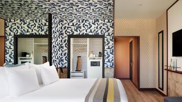 Une chambre d’hôtel comprenant un grand lit, une armoire, une coiffeuse avec un miroir, une petite salle de bain avec un lavabo et des toilettes, et un téléviseur fixé au mur.