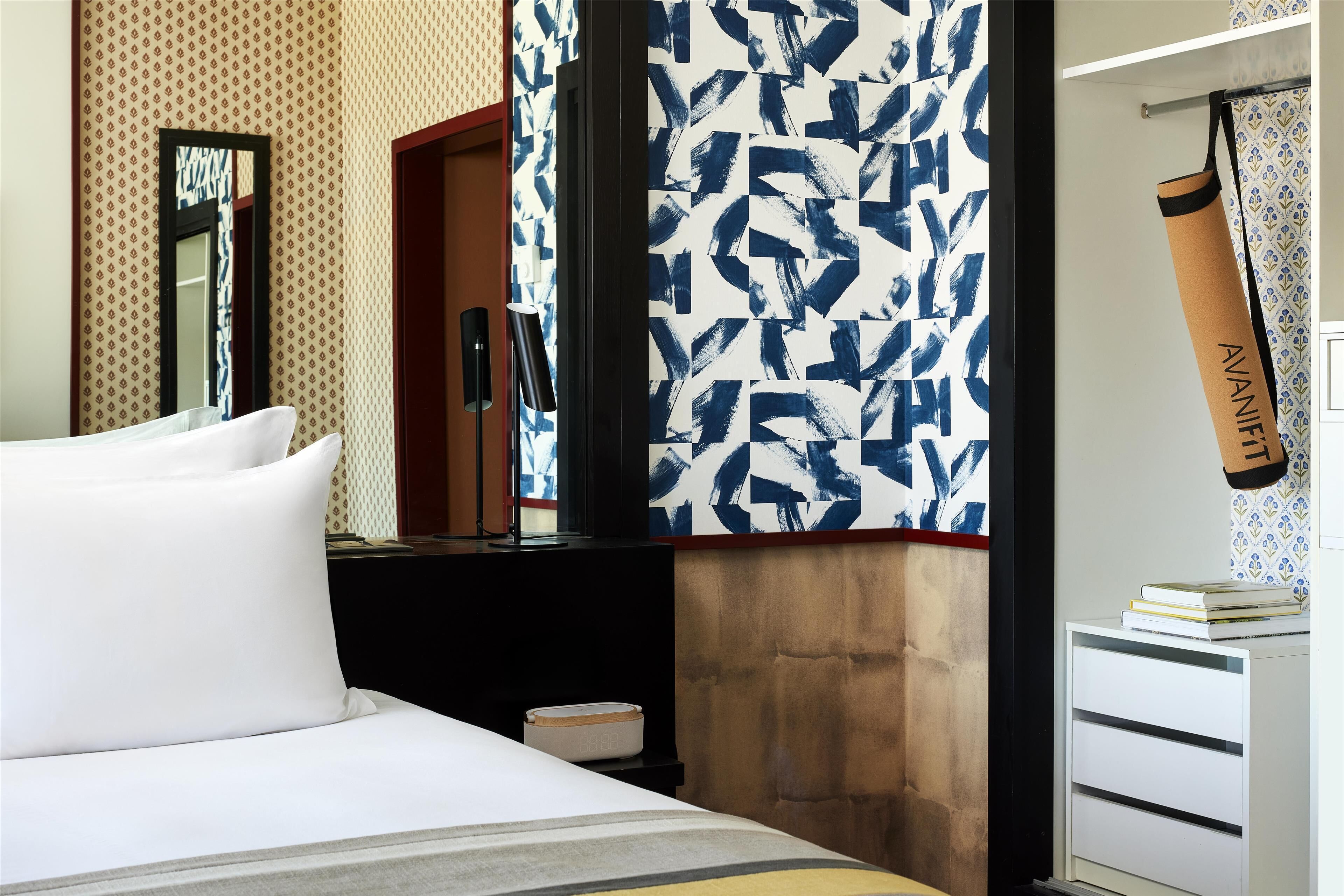 A hotel room with a bed, a nightstand, a mirror, a wardrobe, and a patterned wall.