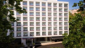 Un hotel de varios pisos con un llamativo letrero de "AVANI", con una cuadrícula de ventanas y balcones, y una fachada plana.