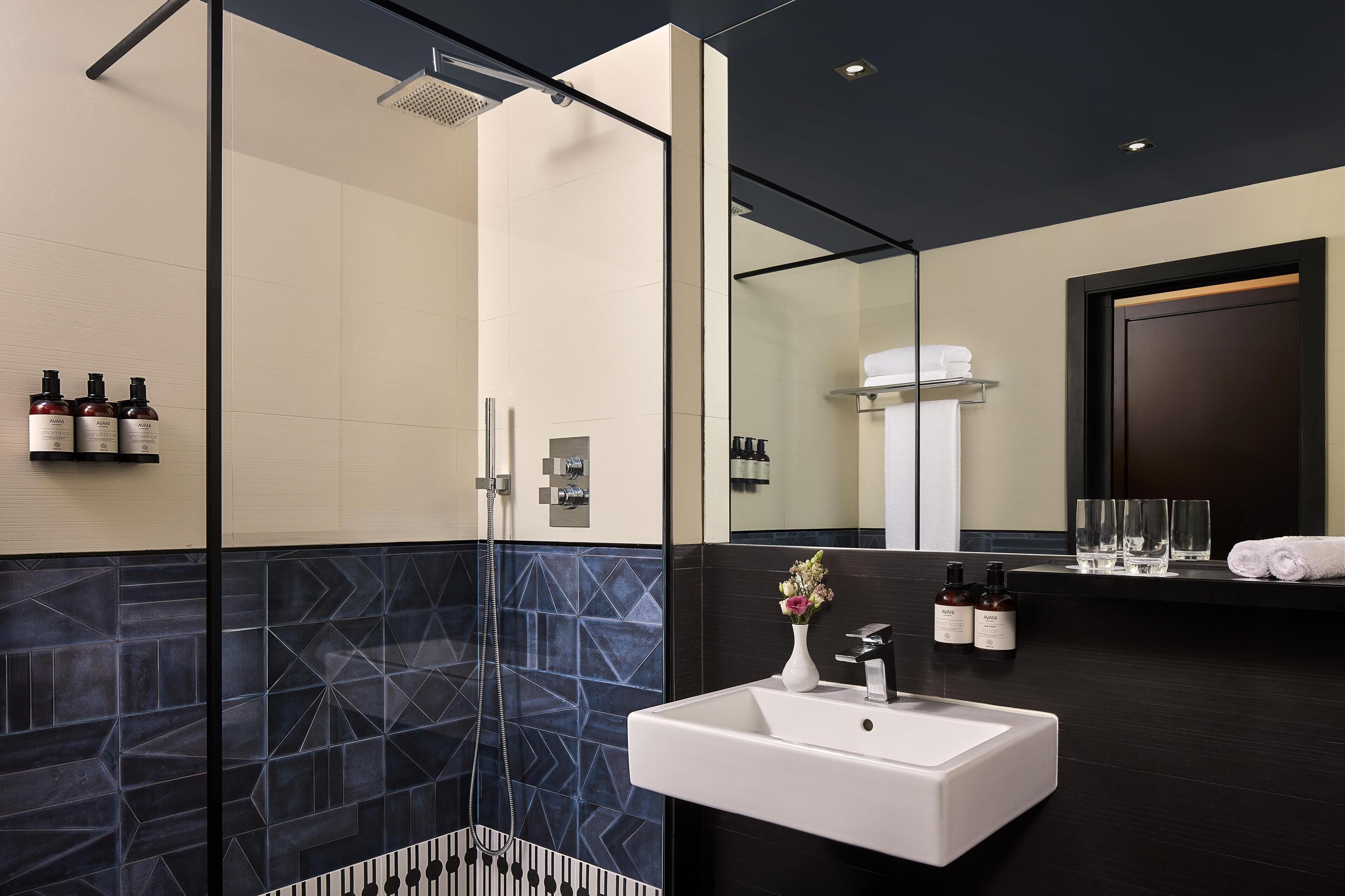 A modern bathroom with a glass-enclosed shower, a white sink, and a dark tiled wall.