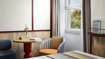 Ein modernes Zimmer mit einem runden Holztisch, einem gemusterten Sessel, einem blauen Sofa und einem Bett mit gestreifter Kopfteil.