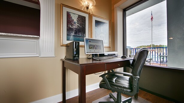 A home office with a desk, computer, and chair. There are two framed pictures on the wall, a window with an American flag, and a view of a pool outside.