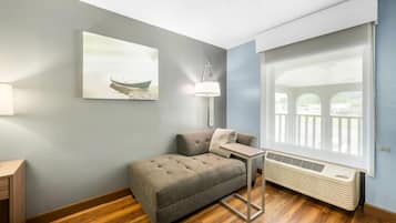 Una habitación con un sofá, una mesa, una lámpara, una ventana con persianas y un cuadro en la pared.