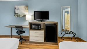 A hotel room with a bed, desk, TV, microwave, refrigerator, chair, and a painting on the wall. - Quality Inn (Barbourville)