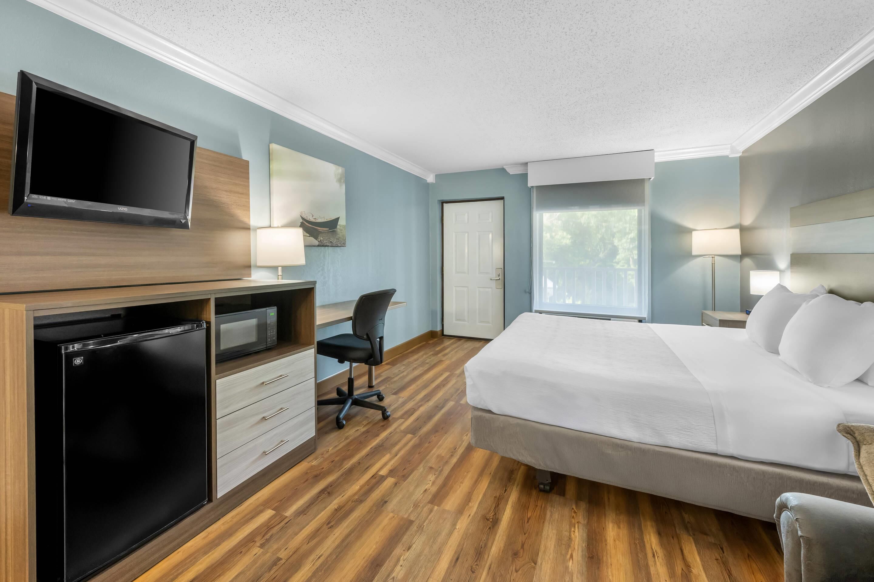 Une chambre d’hôtel équipée d’un lit, d’un bureau, d’un réfrigérateur, d’un four à micro-ondes, d’une télévision et d’une porte.