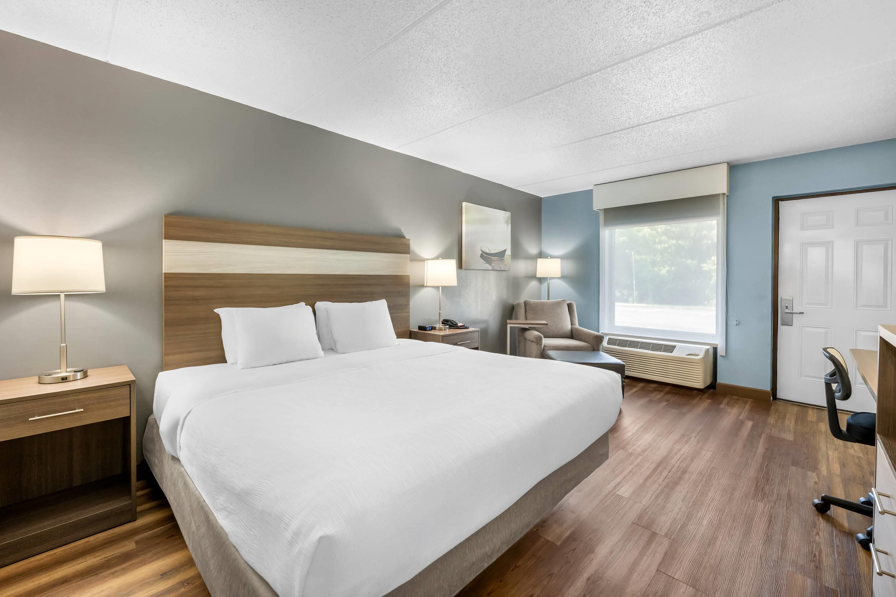 A hotel room with a large bed, bedside tables, a chair, a desk, and a window.