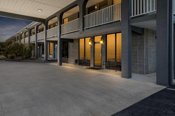 A hotel with a covered outdoor area, multiple balconies, and a seating area with chairs.