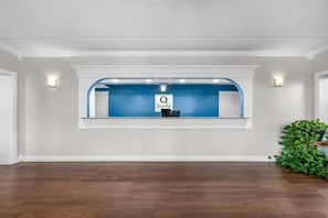 Un espace d’accueil avec un comptoir bleu, une enseigne indiquant « Qualité par Q » et une plante en pot placée à droite.