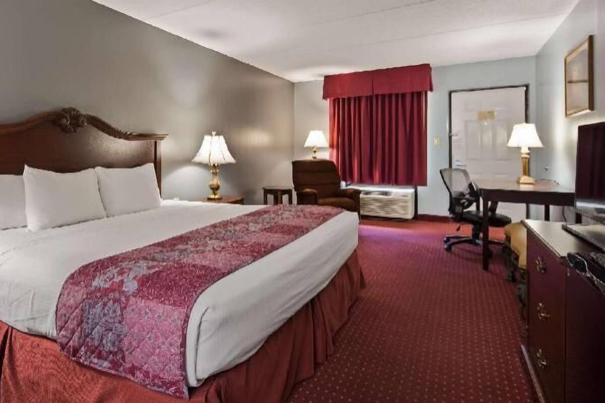 A hotel room with a large bed, two bedside tables, a desk, a chair, and a wardrobe.