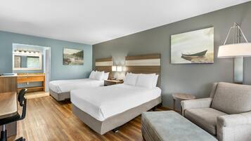 A hotel room with two beds, a desk, a chair, a lamp, and artwork on the walls.