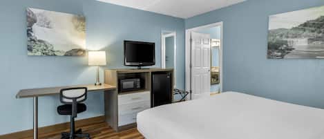 A hotel room with a bed, desk, TV, microwave, and refrigerator.