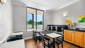 A modern dining area with tables and chairs, a kitchen counter, and a large window offering a view of the outdoors. - Quality Inn (Barbourville)
