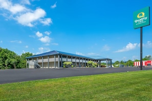 A motel with a blue roof, covered parking, and a sign for Quality Inn by Choice Hotels.