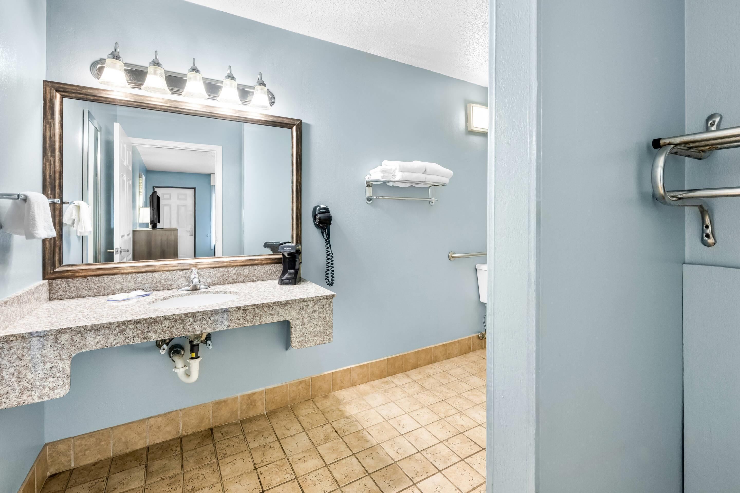 A bathroom with a sink, mirror, towel rack, and a shower area.