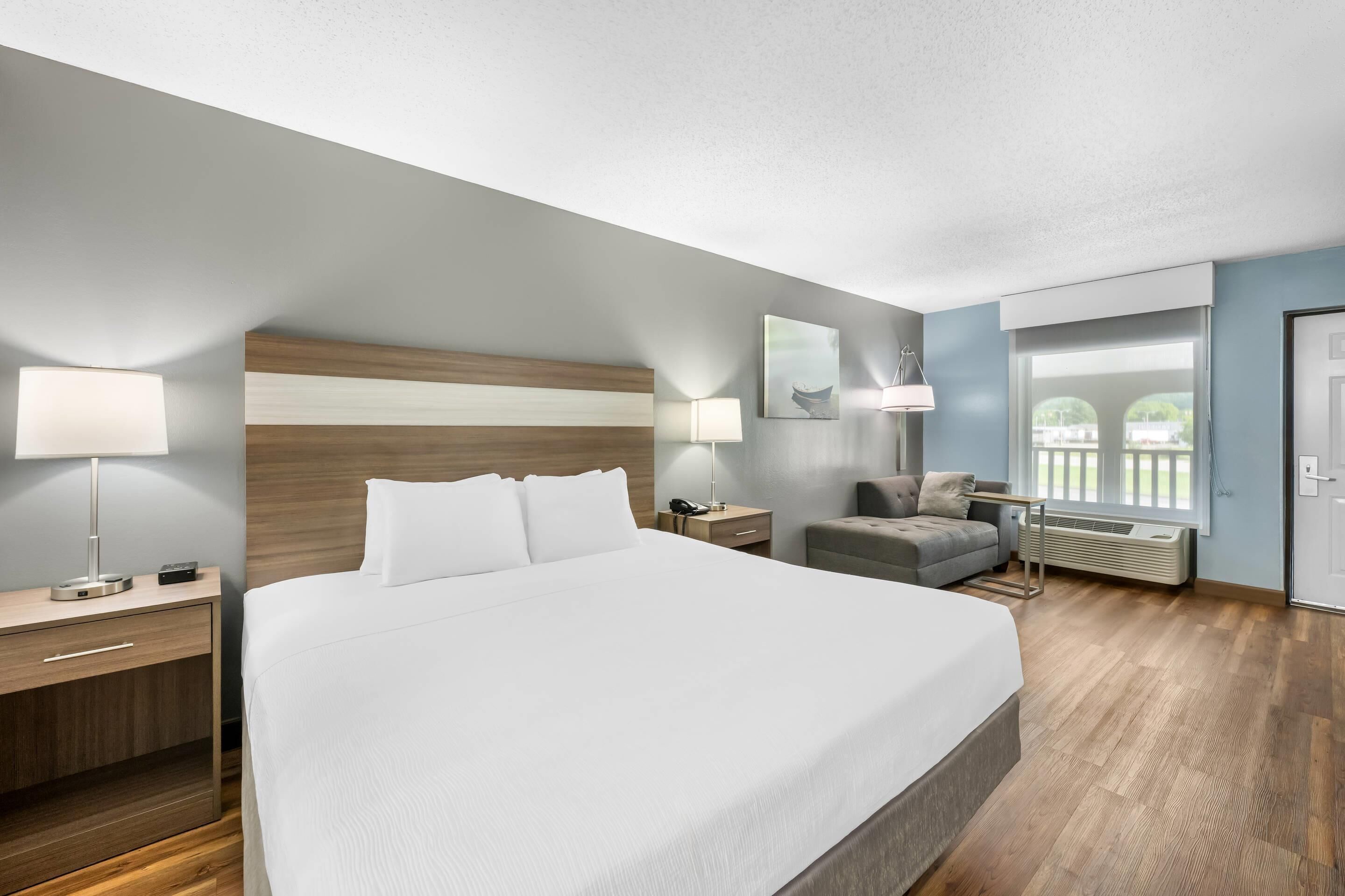 A hotel room with a large bed, bedside tables, a desk, a chair, a window with a view, and a door.