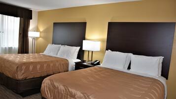 Habitación de hotel con dos camas, cada una con cubrecama marrón, almohadas blancas y una mesita de noche con lámpara y teléfono.