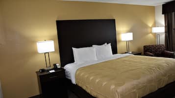 Een hotelkamer met een groot bed, twee bedlampen, een bureau met telefoon en een stoel.