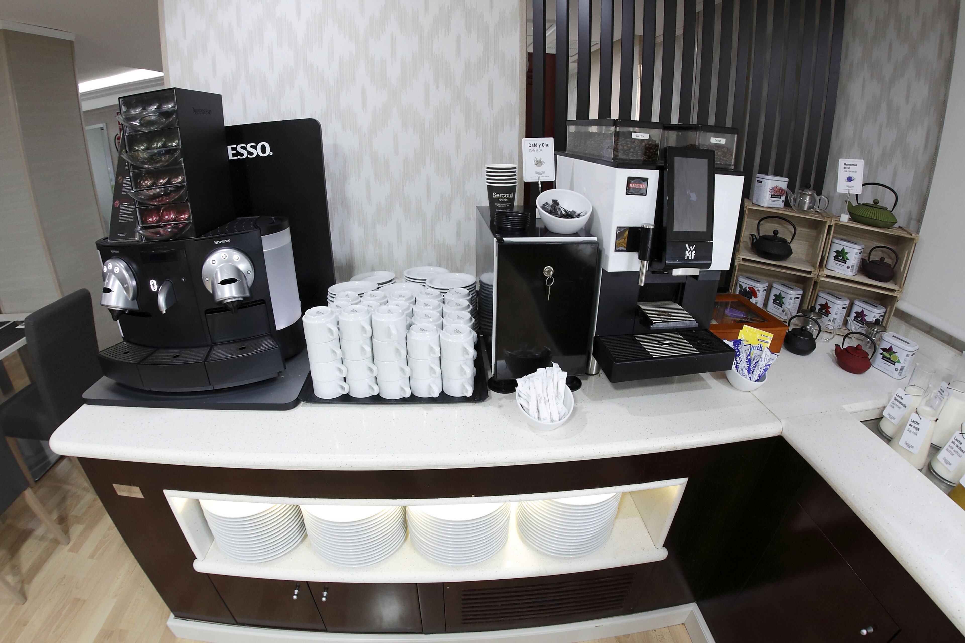 A coffee station with multiple espresso machines, a coffee grinder, and a variety of coffee cups and saucers.