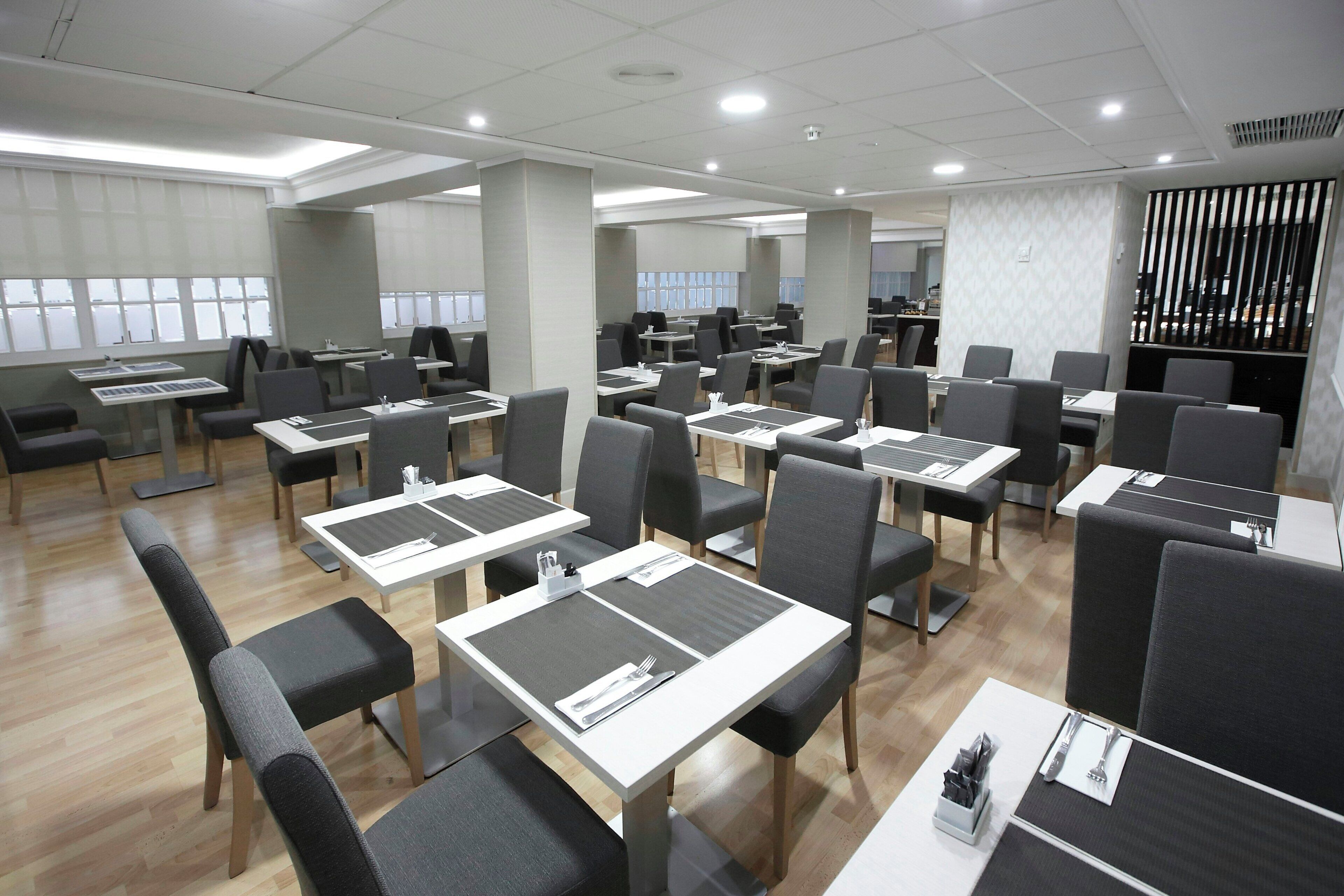 Un comedor moderno con varias mesas y sillas, vistas al exterior a través de amplios ventanales, y un separador con listones verticales.
