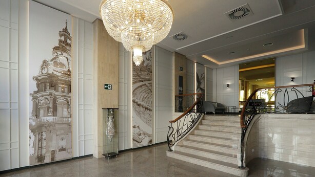 A grand staircase with a chandelier, a wall with a building mural, and a modern interior design.