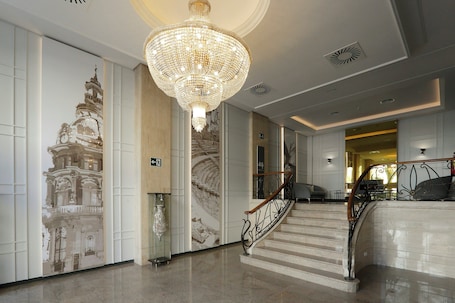 A grand staircase with a chandelier, a wall with a building mural, and a modern interior design.