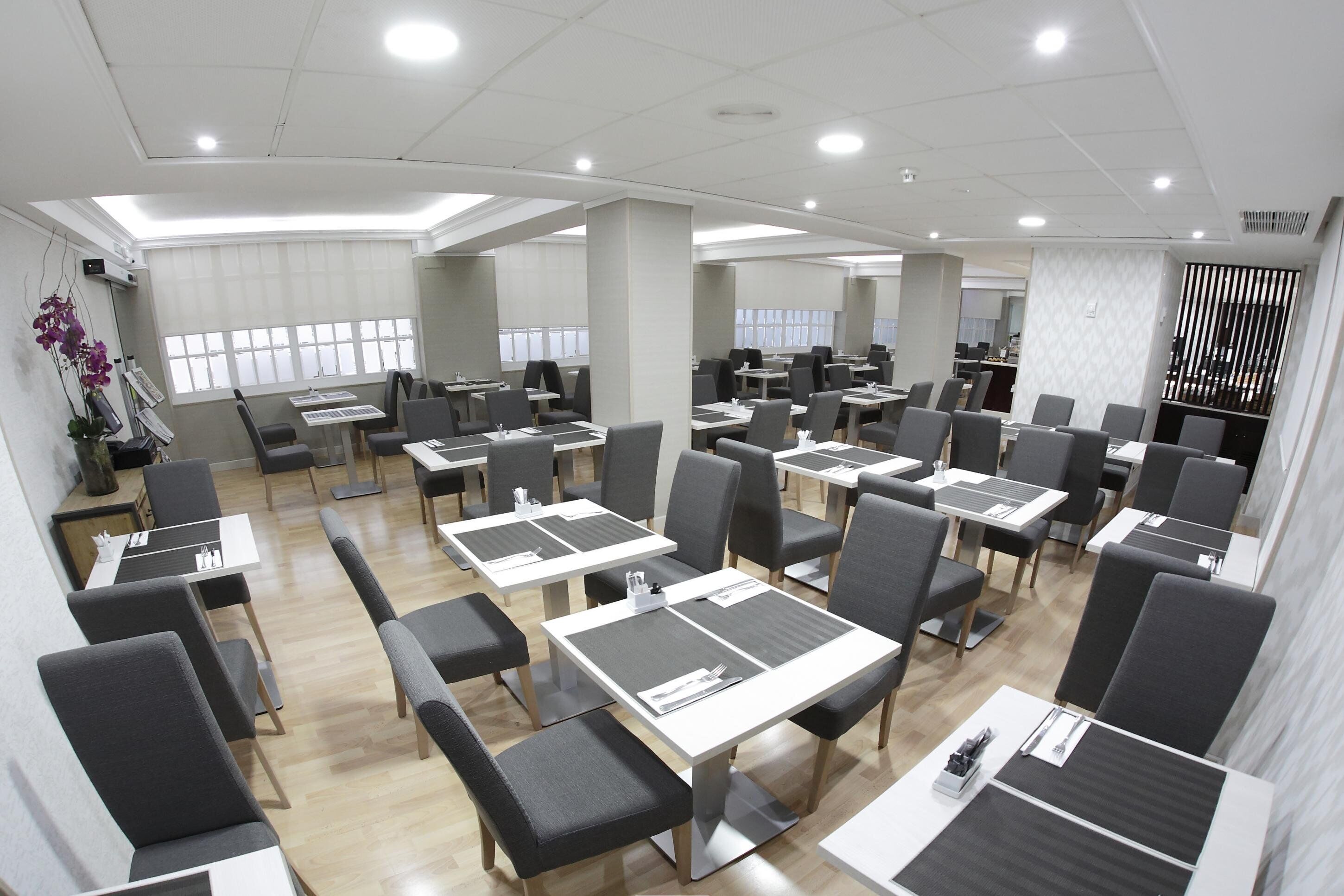 A modern dining area with multiple tables and chairs, large windows, and a clean, well-lit interior.