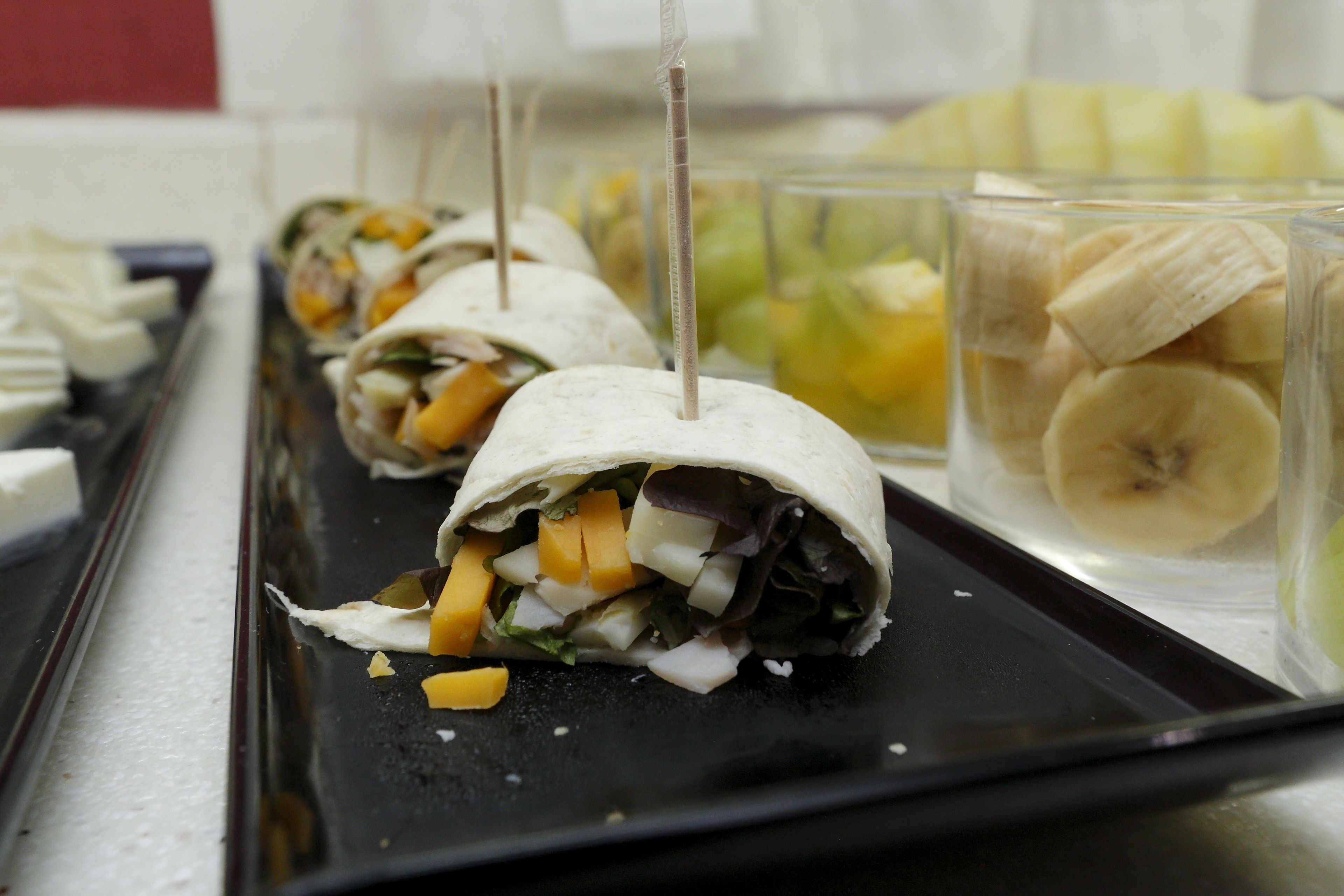 A tray of food items, including wraps and sliced bananas, on a table.