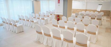 A conference room with rows of white chairs with brown sashes, a whiteboard, and a fire extinguisher.