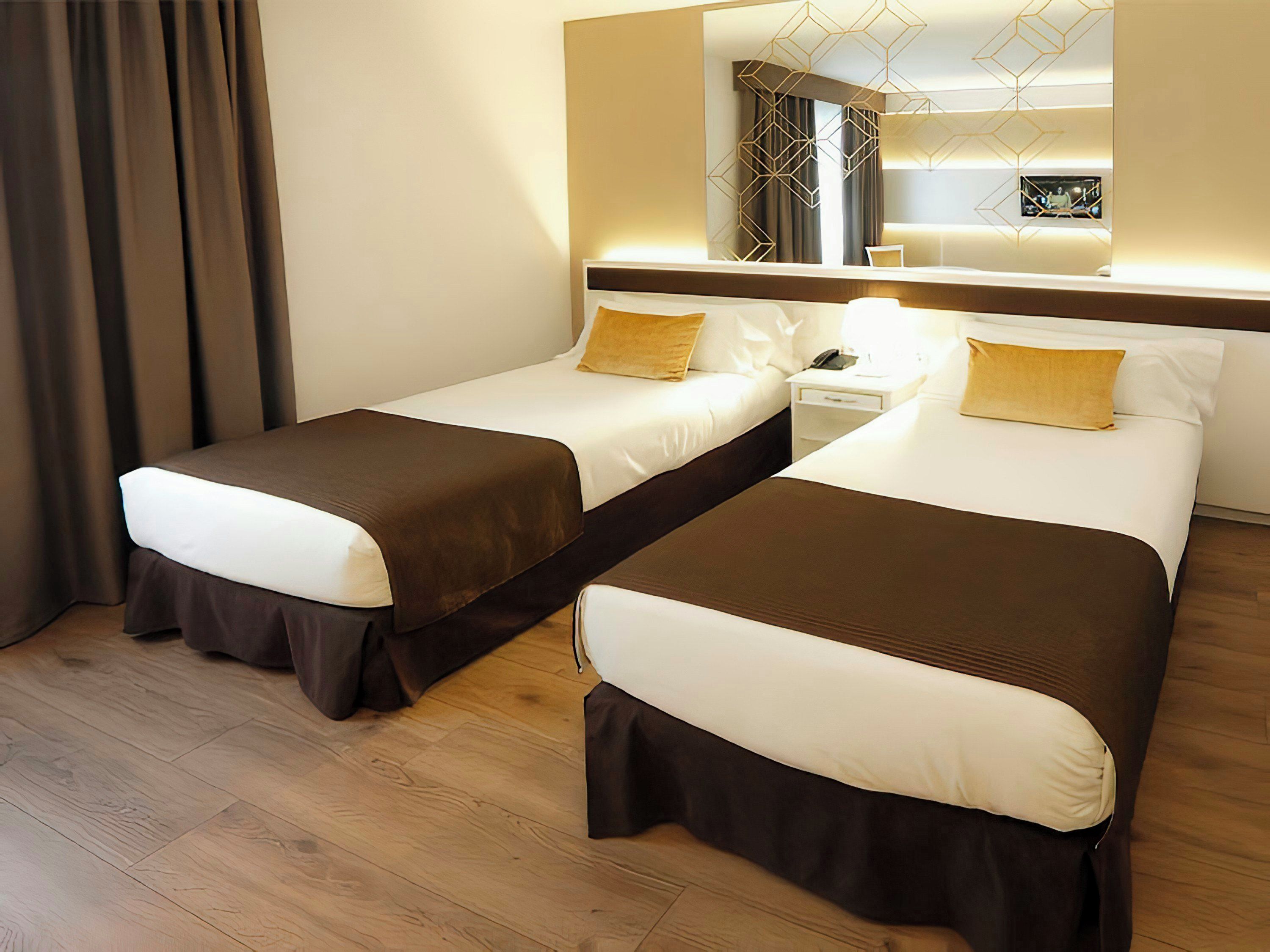 Ein Hotelzimmer mit zwei Betten, einem Nachttisch mit Lampe, einem Spiegel und einem geometrischen Leuchten.