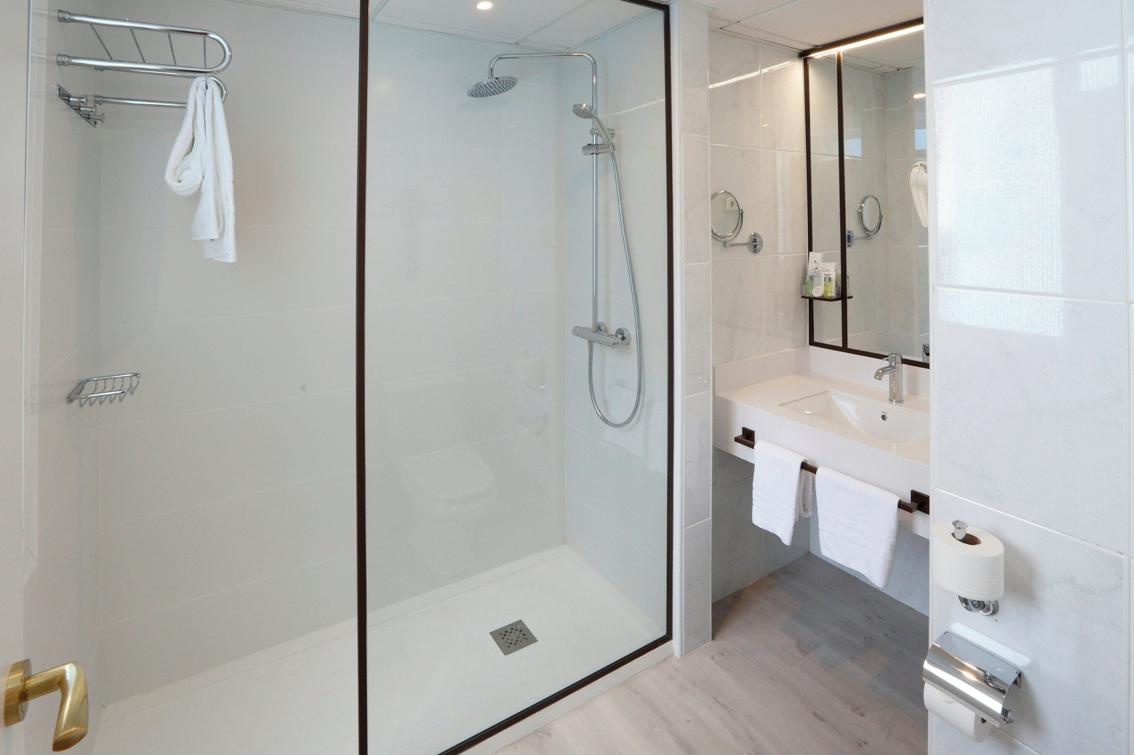 Un baño moderno con ducha acristalada, lavabo blanco y un espejo grande.