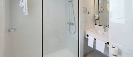 Un baño moderno con ducha acristalada, lavabo blanco y un espejo grande.
