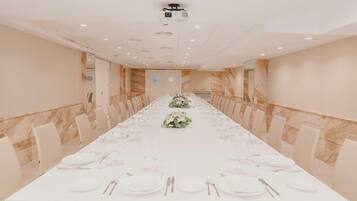 Un salón de conferencias con una larga mesa dispuesta para un evento formal, equipado con un proyector y un espejo grande en la pared.