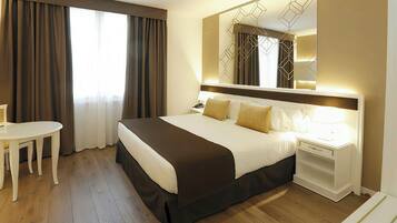 A hotel room with a large bed, bedside table, and a desk with a chair.