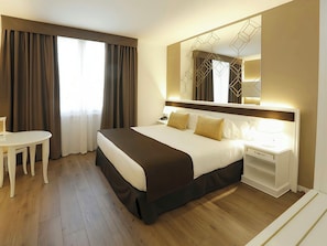Una habitación de hotel con una cama grande, una mesita de noche y un escritorio con una silla.