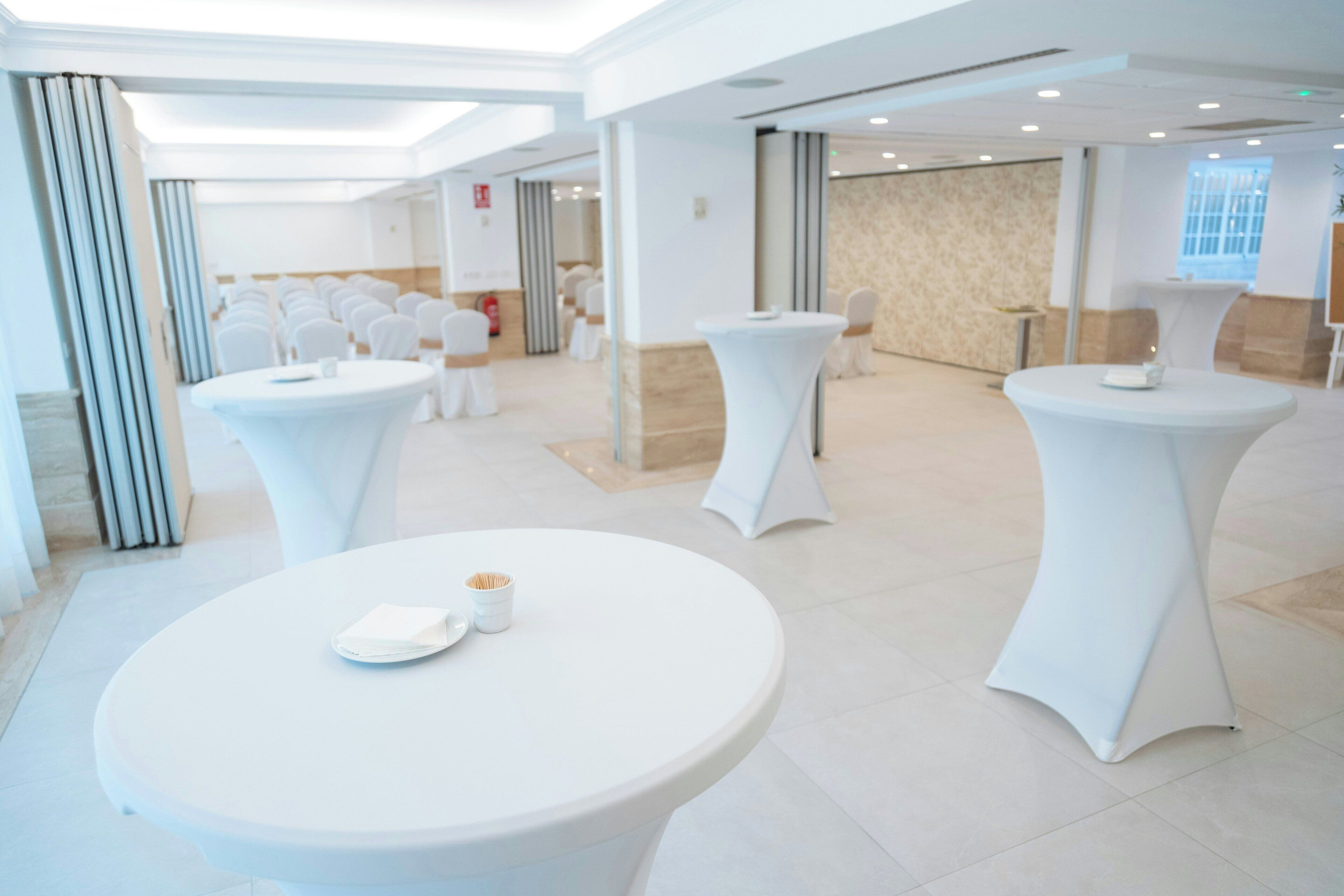 Un rebedor d'hotel modern amb taules rodones, cadires blanques i un paviment de marbre.